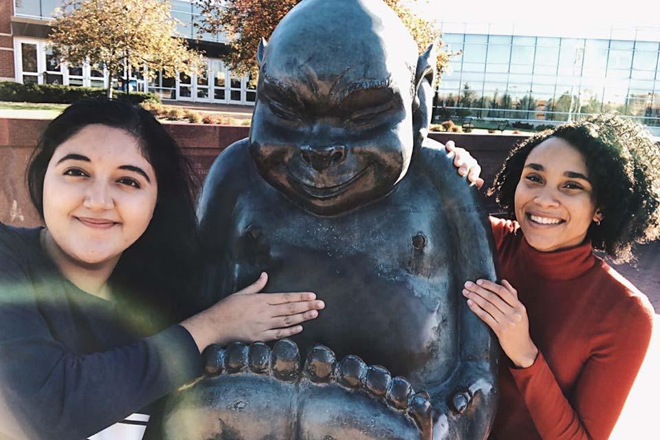 Two students standing at Billiken statue